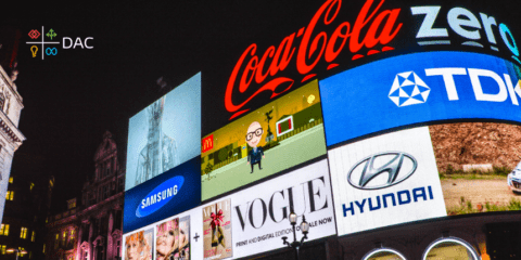 Bright billboard advertisements at night, featuring brands like Coca-Cola, Samsung, Vogue, and Hyundai.