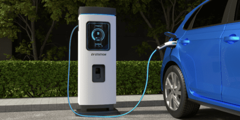 A blue electric car charging at an EV station outdoors.