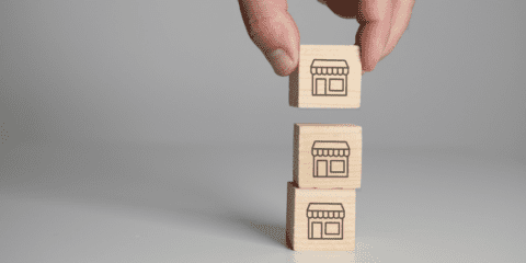 A hand stacking wooden blocks with store icons on them.