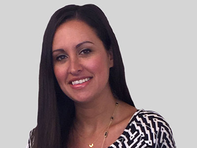 Smiling woman with long dark hair wearing a patterned top.