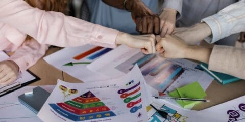 A group of people fist-bumping over a table with various colorful business charts and documents.