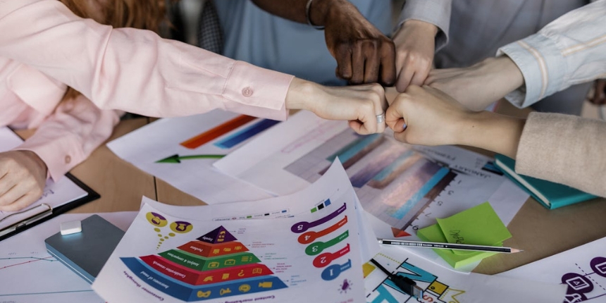 Several people fist bumping over a table with various charts and documents.