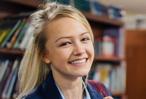 Smiling girl in a school uniform with bookshelves in the background.