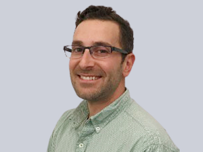 Man wearing glasses and a green button-up shirt smiling.