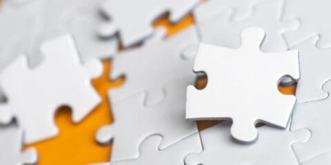 White puzzle pieces with one piece standing out on an orange background.