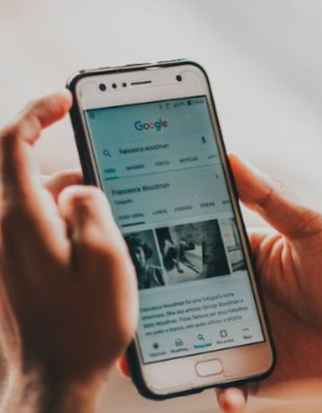 A person holding a smartphone with a Google search results page displayed on the screen.