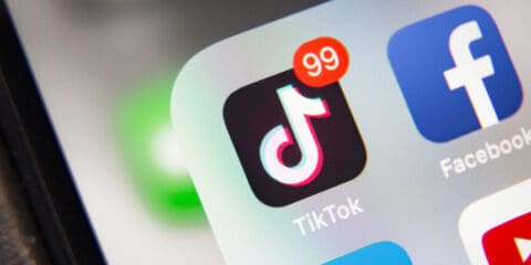 Close-up of a smartphone screen showing the TikTok app icon with 99 notifications next to other app icons.