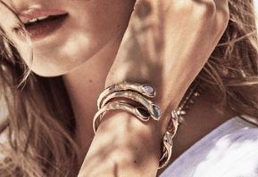 A woman's wrist adorned with gold bracelets featuring colorful gemstones.