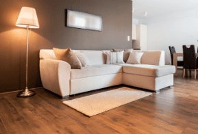 Living room with a beige sectional sofa, floor lamp, small rug, and wooden flooring.