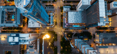 Aerial view of a city intersection surrounded by tall buildings and streetlights at dusk.