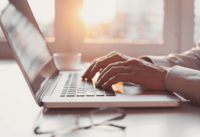 Person typing on a laptop with sunlight coming through a window.