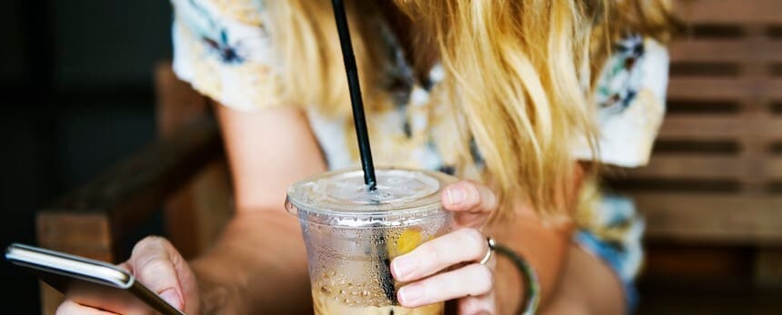 Person drinking iced coffee through a straw and using a smartphone.