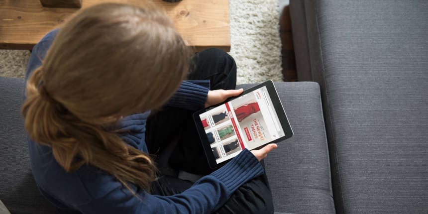 Blond woman is sitting on sofa and is shopping online for clothes from home