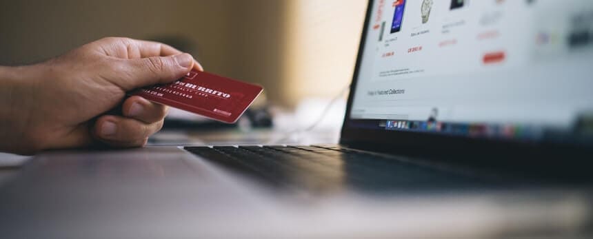 Hand holding a credit card in front of a laptop displaying an online shopping website.