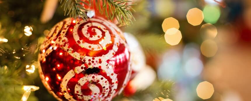 Red and gold Christmas ornament on a tree with blurred festive lights in the background.