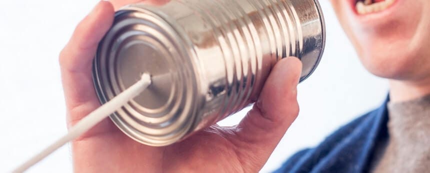 A person holding a tin can attached to a string, speaking into it.