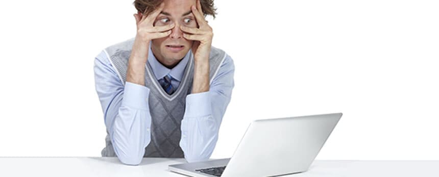 A frustrated man sitting at a desk, gazing at a laptop.