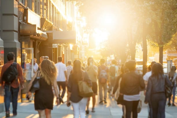 Crowd of anonymous men and women walking down an urban sidewalk with bright glowing sunlight in the background on a busy street in downtown Manhattan, New York Cit