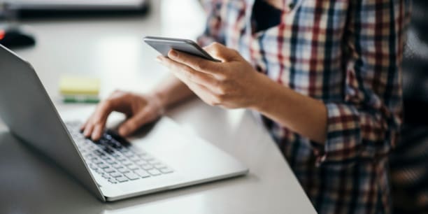 Nahaufnahme einer jungen Frau mit Smartphone und Laptop am Bürotisch