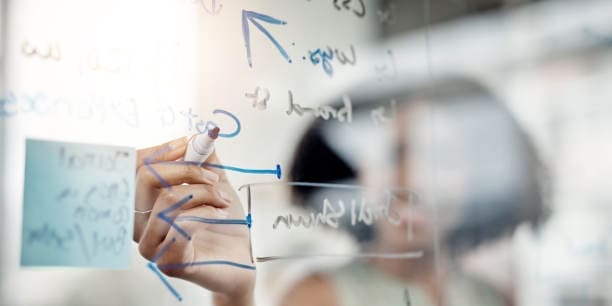 Ausschnitt einer nicht erkennbaren jungen Geschäftsfrau, die in ihrem Büro an einem Glas-Whiteboard arbeitet