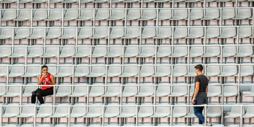 One woman sitting and one man is walking to his seat on a stadium bleachers.