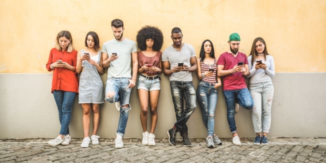 Multiracial friends using smartphone against wall at university college backyard - Young people addicted by mobile smart phone - Technology concept with always connected millennials