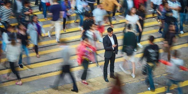 High angle view of businessman using smart phone amidst crowd. Professional is standing on busy street. He is surrounded by people in city.