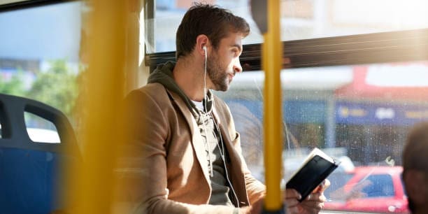 Cropped shot of a handsome young man reading a book during his morning bus commute