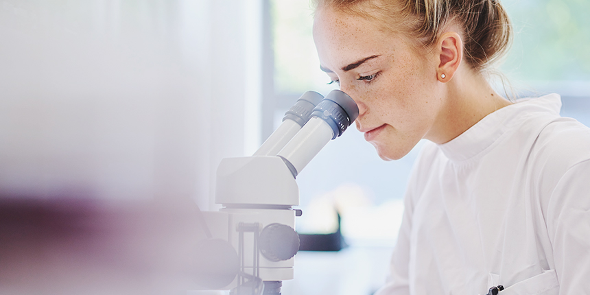 Femme en blouse de laboratoire regardant dans un microscope