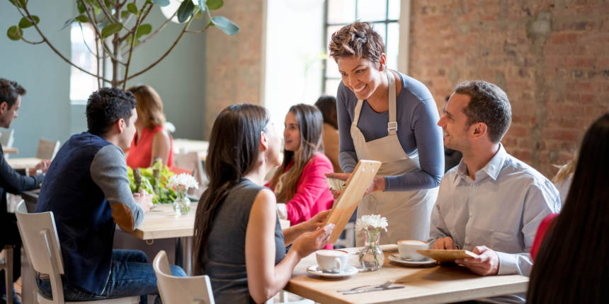 Friendly waitress serving couple at a restaurant taking orders and looking very happy