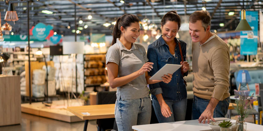 Cheerful sales woman showing a design on tablet to mid adult couple looking for furniture at a home store - Home renovation concepts