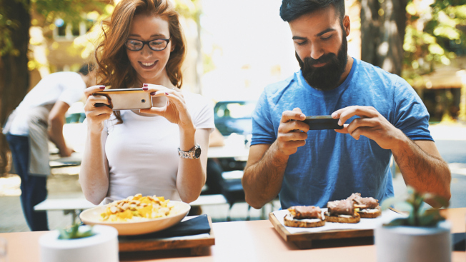 Closeup front view of a couple at a restaurant taking shots of their meal in order to post it online. It's seems very strange if you do not do this nowadays.