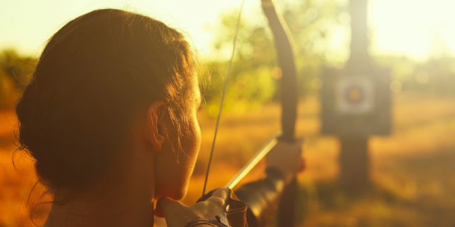 Female archer in the field at sunset